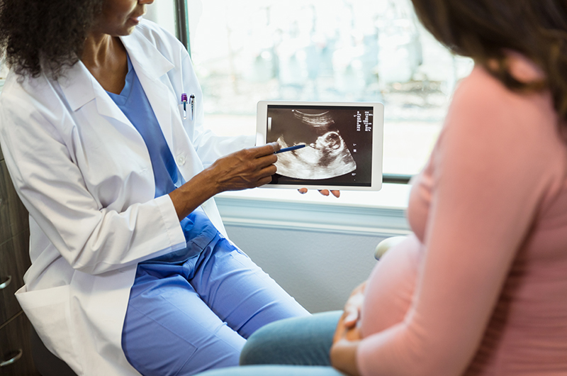 A pregnant mother receives improper prenatal care from her female doctor as they review an ultrasound in the doctor's office.
