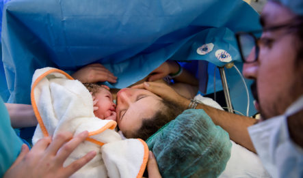 A woman holds her baby in a hospital gown after a botched c-section.