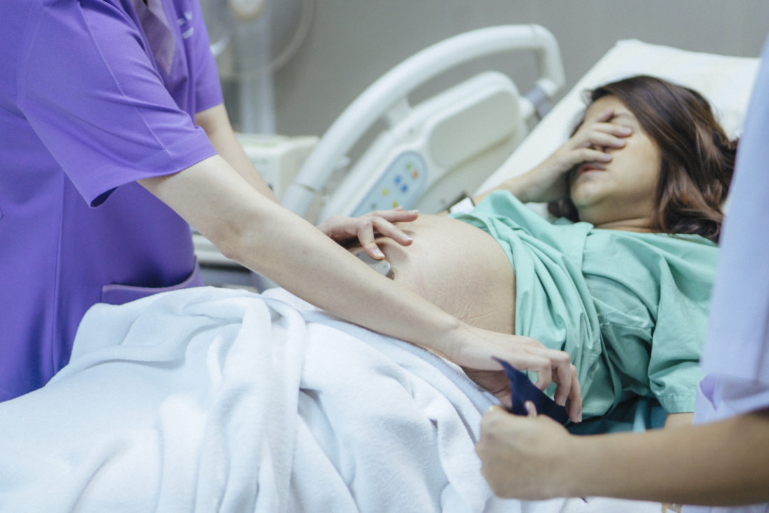 A pregnant woman holds her face in her hand as a nurse performs a check up on the child, upset due to an issue that may lead to a birth injury lawsuit.