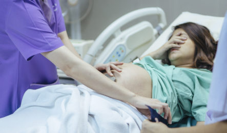 A pregnant woman holds her face in her hand as a nurse performs a check up on the child, upset due to an issue that may lead to a birth injury lawsuit.