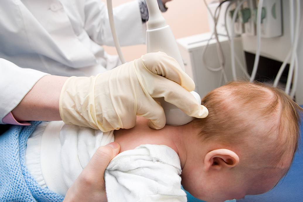 A baby laying on its belly being checked by a doctor for signs of brachial plexus injury at birth