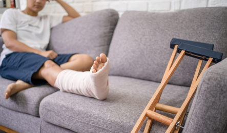 man sitting on couch with crutches and foot in cast thinking about filing a personal injury claim
