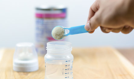 A person puts a scoop of baby formula into a baby bottle, not knowing that certain types of formula can lead to necrotizing enterocolitis.