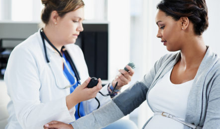 A pregnant woman has preeclampsia during pregnancy, and is in a doctor's office getting her blood pressure checked by the physician.