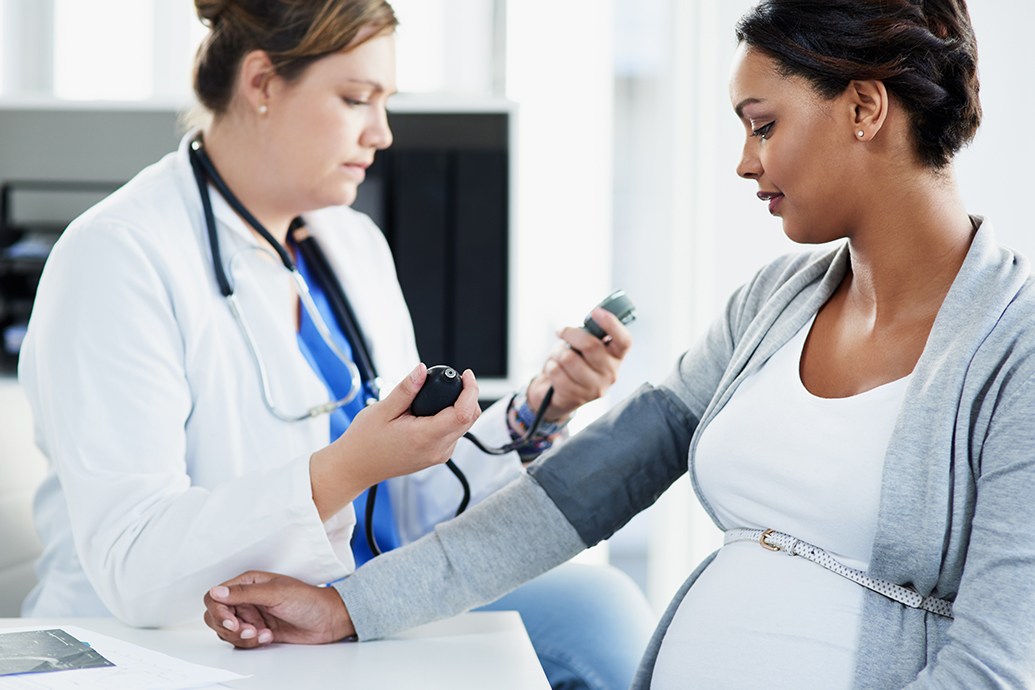 A pregnant woman has preeclampsia during pregnancy, and is in a doctor's office getting her blood pressure checked by the physician.