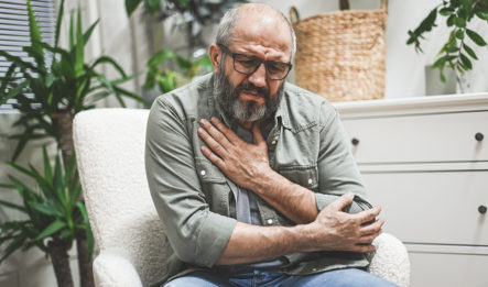 man sitting in chair holding arm to chest after experiencing one of the causes of a pulmonary embolism