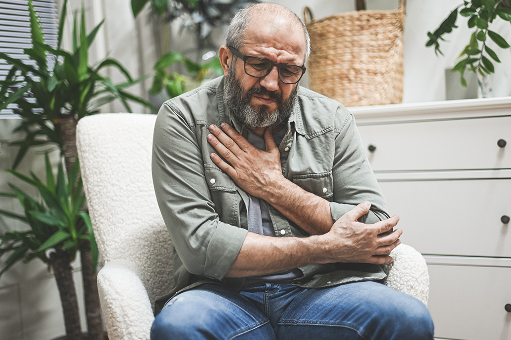 man sitting in chair holding arm to chest after experiencing one of the causes of a pulmonary embolism