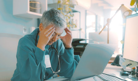 woman leaning over her desk with hands on her head looking stressed